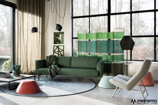 Modern kantoor met groen zitbank, crèmekleurige fauteuil, rode poef, glazen boekenkast, zwarte hanglampen en grote ramen met
