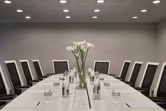 Moderne vergadertafel in wit met zwart-witte gestreepte ergonomische bureaustoel, glazen waterkannen, witte calla's in vaas,