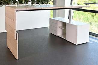 Moderne kantoorreceptie met wit en naturel houten bureau, grijze vloer, zwarte draagbalk, opbergkasten en groene planten.