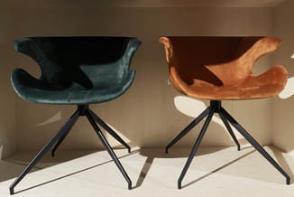 Twee design stoelen met uitgeklapte armsteunen op zwart metalen driepootonderstel. Links donkerblauwe fluweelstoel, rechts or