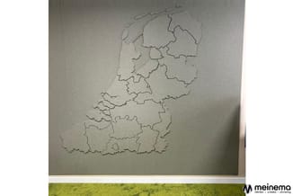 Reliëfkaart van Nederland en België aan witte muur, onderverdeeld in provincies en regio's met erbovenuit komende grenzen.