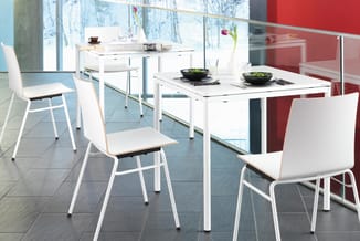 Witte eettafel met vier witte stoelen met houten zitting in moderne kantoorruimte met rood en blauw accent, grote ramen met s