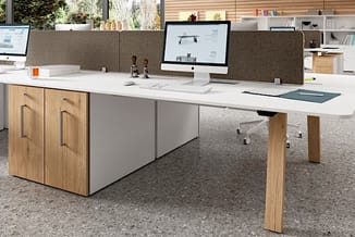 Moderne kantoorwerkplek met wit blad en houten poten, grijze akoestische schermen, wit onderkastje en houten kasten.
