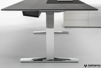 Moderne vergadertafel met zwart blad, zilverkleurige zuilvormige poot en wit onderstel, schuin aanzicht in kantoorruimte.