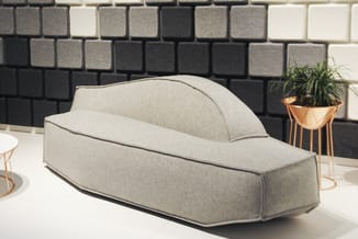 Grijze loungebank met hoge rugleuning en zwarte biezen in modern interieur met bakstenen muur en plantenbak.