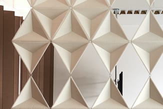 Witte driedimensionale akoestische wandpanelen in geometrisch patroon, met bruine deur links en zwarte deurkruk rechts zichtb