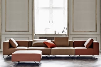 Modulaire bruine zitgroep met chaise longue en ottoman, metalen poten, in klassieke ruimte met hoge ramen en panelwanden.
