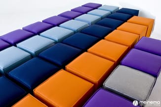 Gekleurde zitkubussen in paars, lichtblauw, donkerblauw, oranje en grijs, opgesteld in rijen op een witte achtergrond.