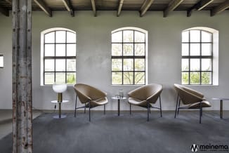 Moderne lounge met drie taupe leren stoelen met zwart stalen frame, witte tafels, industriële betonnen zuil en drie grote raa