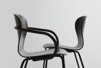 Moderne stoel met grijs gebogen kunststof zitting en zwart metalen frame, side-on weergegeven tegen witte achtergrond.