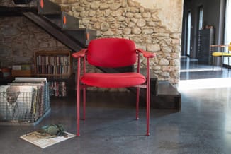 Rode designstoel met armleuningen en metalen frame in industriële kantoorruimte met stenen muur.