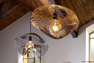 Twee hangende draad-designlampen met gouden en zwarte weefstructuur in een ruimte met houten plafond en witte wanden.