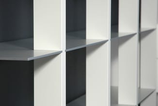 Moderne witte kasten met zwarte nissen en grijze planken tegen donkere wand, zonnelicht werpt schaduw.