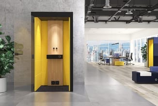 Gele belcel met houten deur in modern kantoor met betonnen wanden, werkplekken en uitzicht op skyline.