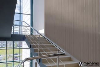 Moderne trap met stalen trapleuning en horizontale kabels in heldere kantoorruimte met grote ramen en grijze wandbekleding.