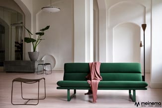 Groene modulaire bank met roze plaid in minimalistisch interieur met houten vloer, witte wanden en designmeubels.