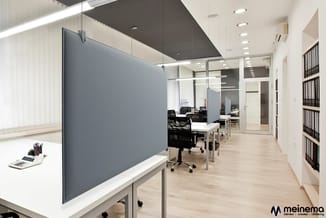 Modern kantoor met grijze akoestische wand, witte werkblad, houten vloer, glazen scheidingswanden, zwarte bureaustoel en boek