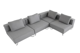 Grijze modulaire bank met hoekopstelling, losse kussens en metalen poten op witte achtergrond.