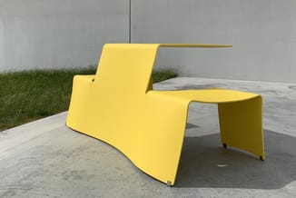 Gele moderne loungefauteuil met bijzettafel, organische vormen, buiten op betonnen terras tegen grijze muur.
