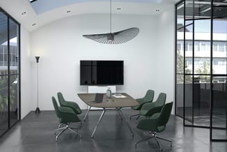 Moderne vergaderruimte met ovale tafel, vier groene stoelen, wandmontage TV, hangende design lamp en raampartijen met zicht o