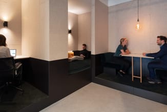 Modern kantoor met grijze panelwanden, zwarte werkplekken met bureaustoelen, zithoek met geel kussen, vergadertafel en hangla