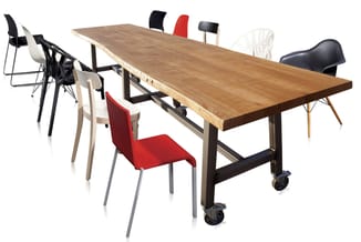 Houten vergadertafel met zwenkwielen en diverse stoelen in zwart, rood, wit en beige om de tafel geplaatst.