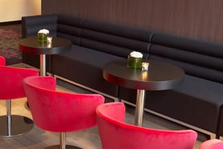 Moderne lounge-opstelling met zwarte ronde tafels met rode rand, rode fluweelachtige stoelen, zwarte bank en witte bloemen in