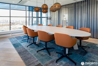 Moderne vergaderkamer met ovale witte tafel, oranje bureaustoel met zwart onderstel, hangende bollampen in goud, blauw gestre
