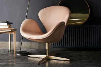 Moderne fauteuil met crème-kleurig bekleding en gouden metalen voet, naast houten bijzettafel in industrieel interieur.