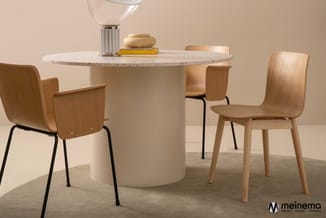 Ronde marmeren tafel met wit onderstel en houten stoelen met zwart metalen poten in neutrale interieurruimte.