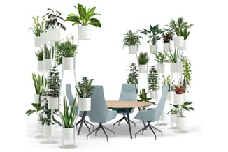 Kantoorruimte met ronde houten tafel, vier blauwe draaistoelen en witte modulaire plantenbakken met diverse groene planten.