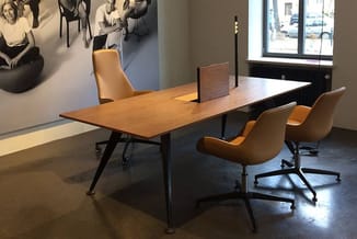 Moderne vergadertafel met houten blad en zwart metalen onderstel, omgeven door drie oranje stoelen met wieltjes in minimalist
