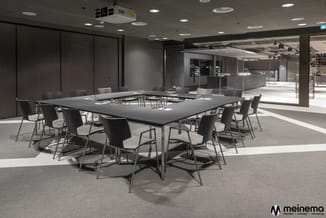 Moderne vergaderruimte met rechthoekige zwarte tafel, grijze stoelen met metalen frames en grijze vloerbedekking, omgeven doo