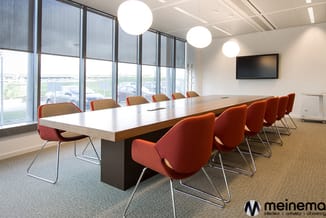Moderne vergaderruimte met lange houten tafel, rode stoelen met metalen onderstel, ronde hanglamps, grote ramen en tv-scherm