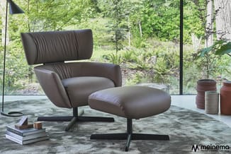 Grijze lederen fauteuil met hoofdsteun en bijbehorende voetenbankje op zwarte poten, in moderne kantoorruimte met raamzicht o