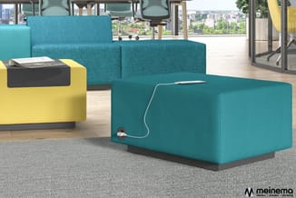 Turquoise pouf met geïntegreerde stroomvoorziening in modern kantoorinterieur met sofa's en uitzicht op stad.