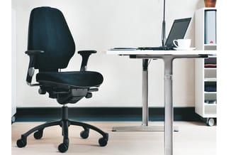 Zwarte ergonomische bureaustoel met armleuningen aan een wit bureau met laptop, naast een wit kastje in een modern kantoor.