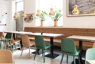 Modern kantoor met witte vergadertafel, groen beklede stoelen, houten wandbekleding, gouden hangende lampen en potplanten bij