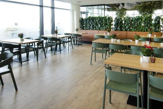Modern kantoor met houten tafels, groene stoelen, bruine zitbanken en groene plantenschermen tegen de wand.