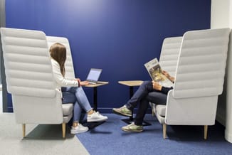 Twee personen zittend in witte gestoffeerde fauteuils met hoge ruggen, tegenover elkaar in een blauwe akoestische ruimte met