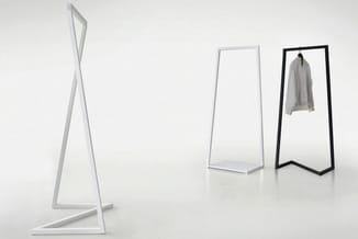 Drie kapstokken met driehoekig frame in wit, wit en zwart, waarvan de rechtse met een grijze jas behangen staat.