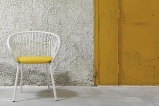 Moderne witte stoel met gele zitting tegen ruwe beige muur en gele deur op betonnen vloer.