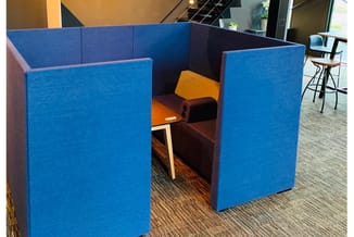 Blauwe akoestische boxen in U-vorm met donkerbruin zitmeubel en oranje kussens in kantoorruimte.