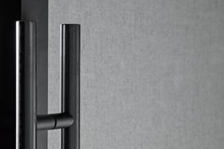 Zwart metalen deurklink op grijze deur, minimalistisch design met twee verticale buizen en horizontale grijpstang.