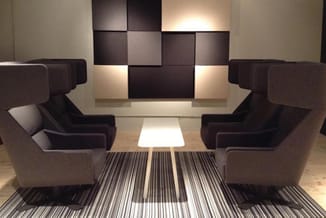 Moderne wachtkamer met twee grijze fauteuils tegenover elkaar, zwarte wandpanelen met verlichting, witte vloerlamp en gestree