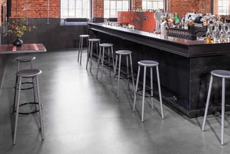 Moderne bar met zwarte bar en zilveren barkrukken. Industriële ruimte met bakstenen muur, betonnen vloer en ramen.