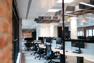 Modern kantoor met zwarte bureaustoelen, witte werkplafonds, gele hangende verlichting, wit kolom en donkere glazen wanden.