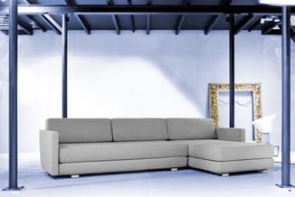 Grijze hoekbank met chaise longue in minimalistisch industrieel interieur met betonvloer en stalen constructie.