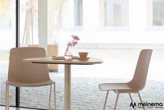 Ronde tafel met beige stoelen in moderne kantoorruimte met grote ramen en uitzicht op water.