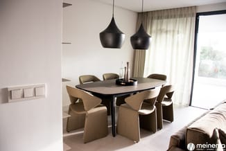 Moderne vergaderruimte met zwarte hanglamp, grijze vergadertafel en zes stoelen in beige stof, grote ramen met gordijnen.